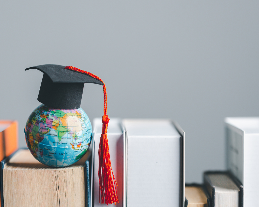 Miniatur-Globus mit Absolventenhut steht auf einem Stapel Bücher – Symbolbild für globale Bildung, Wissenschaft oder akademische Forschung.